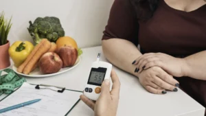Person überprüft Blutzucker neben frischem Obst und Gemüse.